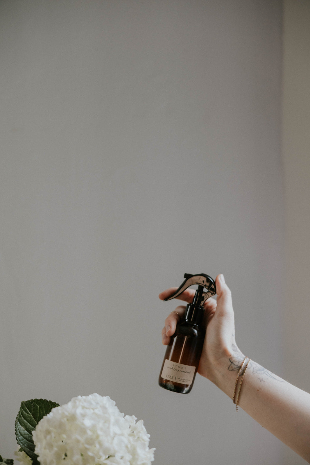 Hand holding a spray bottle with flowers on a neutral background