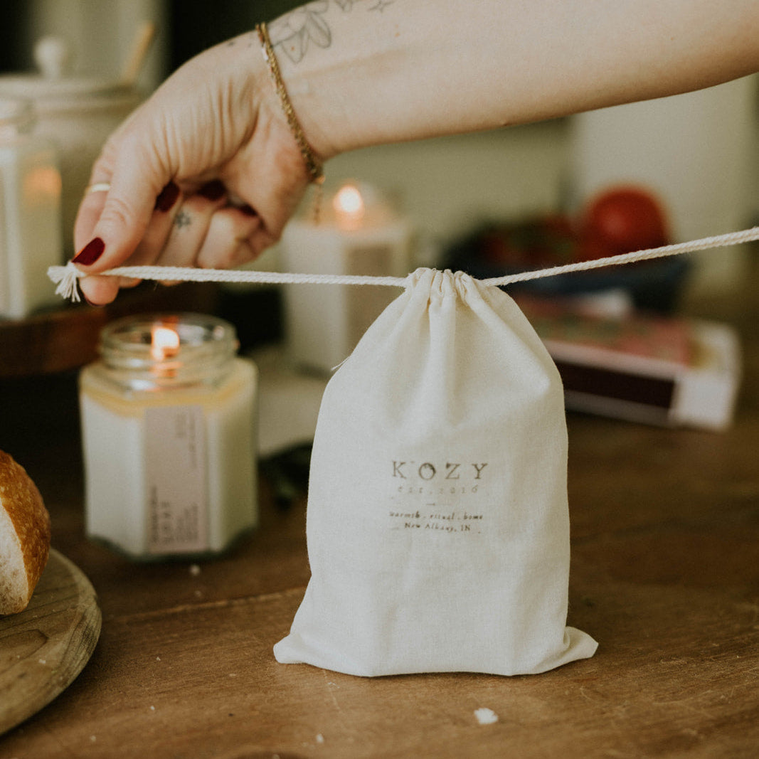 Person holding a drawstring bag labeled 'Kozy' with candles in the background.