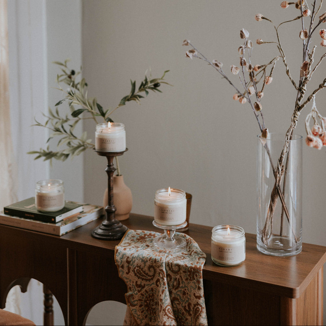 Decorative setup with candles and a vase on a wooden surface against a neutral wall.