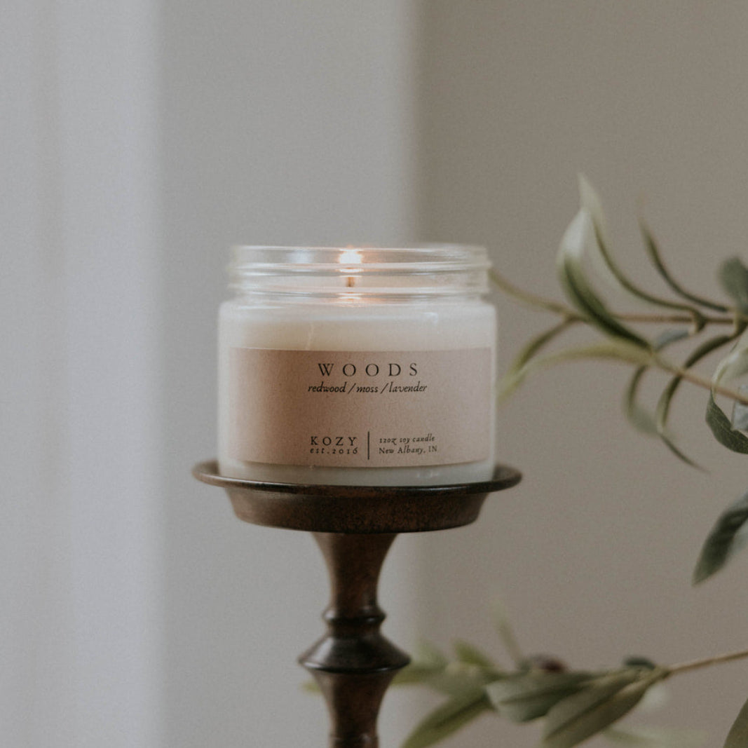 Candle in a wooden holder with a plant in the background
