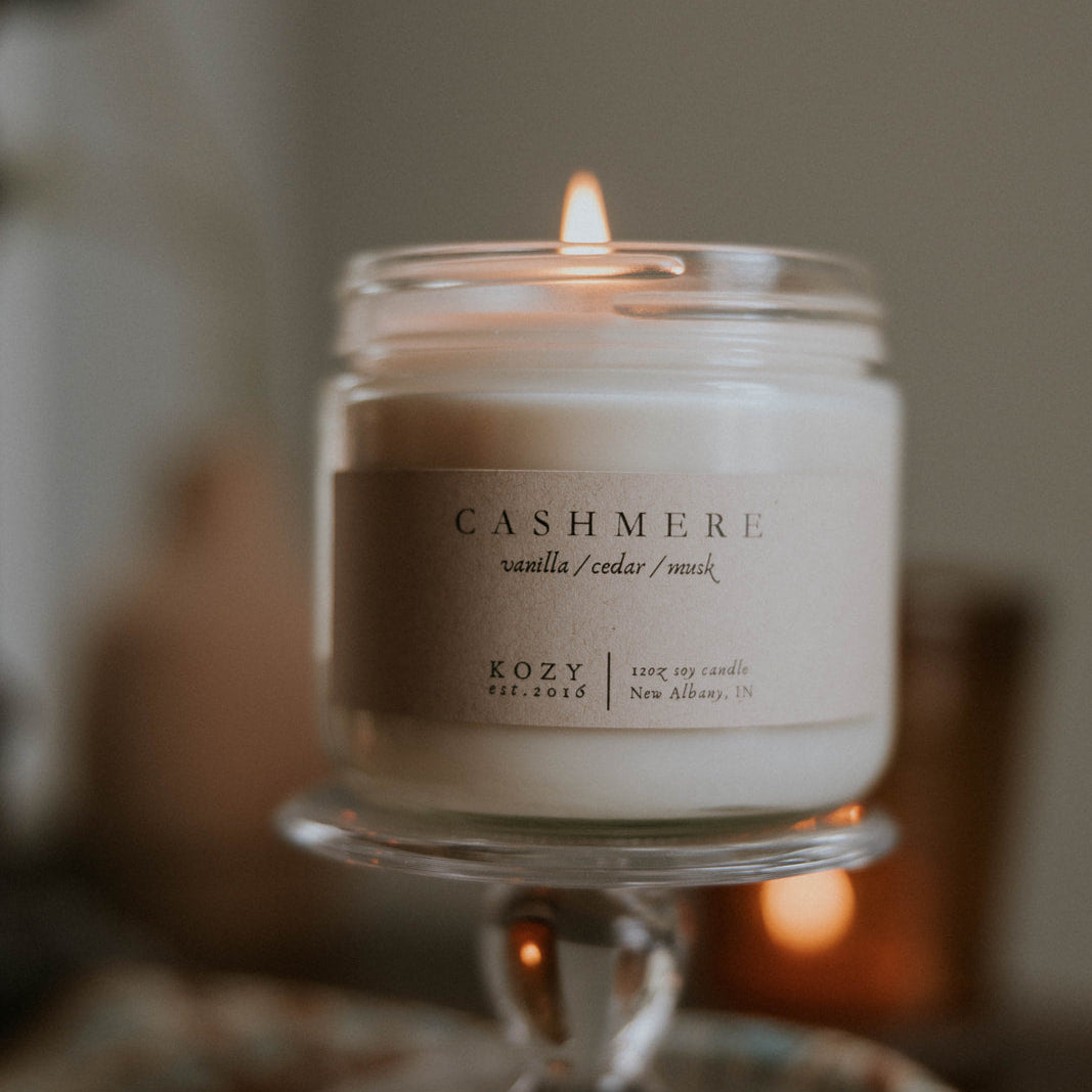 Candle in a glass jar labeled 'Cashmere' on a blurred background