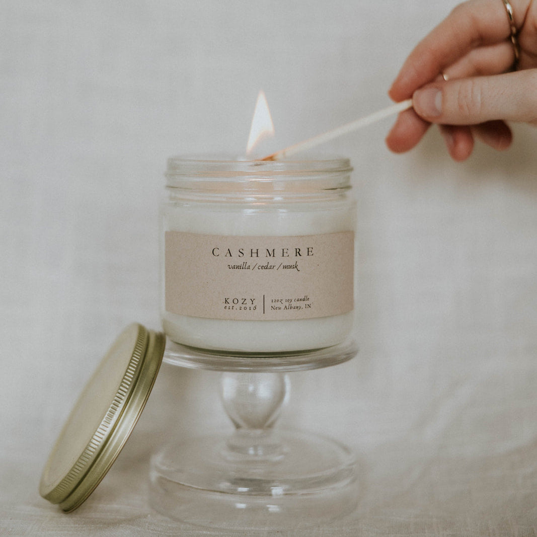 Person lighting a Cashmere candle with a wooden wick, on a neutral background