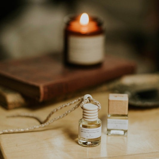 Small car diffuser in the scent 'Autumn Strudel' on a wooden surface, with a lit candle in the background.