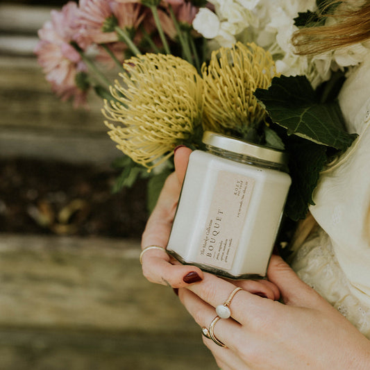 Person holding a candle and a bouquet of flowers with a blurred background