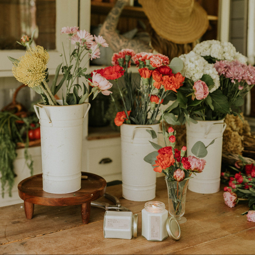 Floral arrangements in white buckets on a wooden table with a rustic background.