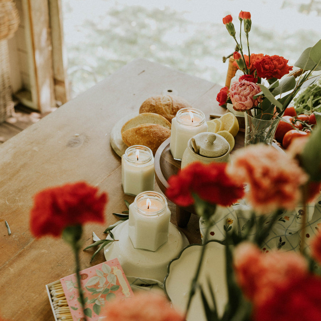 Table setting with candles, flowers, and pastries by a window.