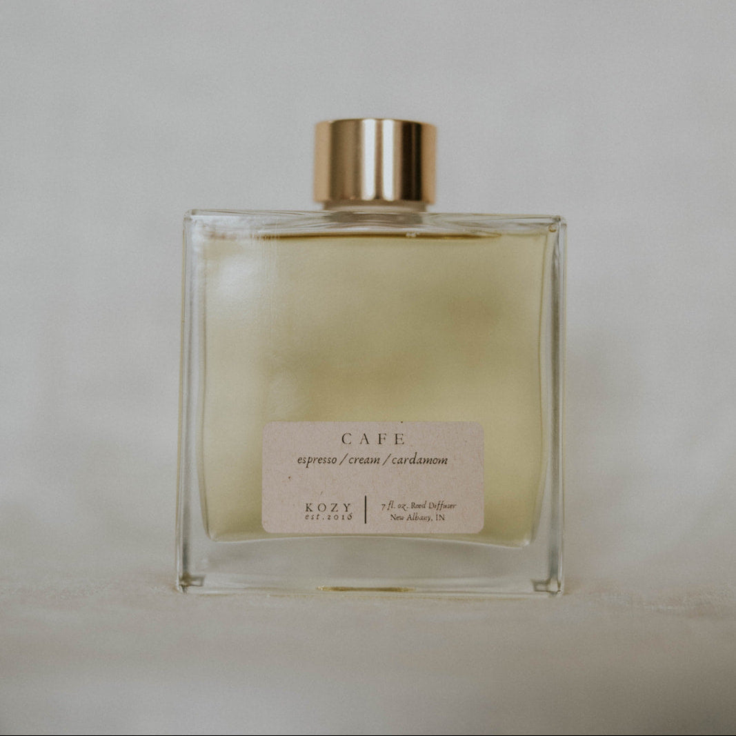 Diffuser bottle scented 'Cafe' with a gold cap on a light gray background