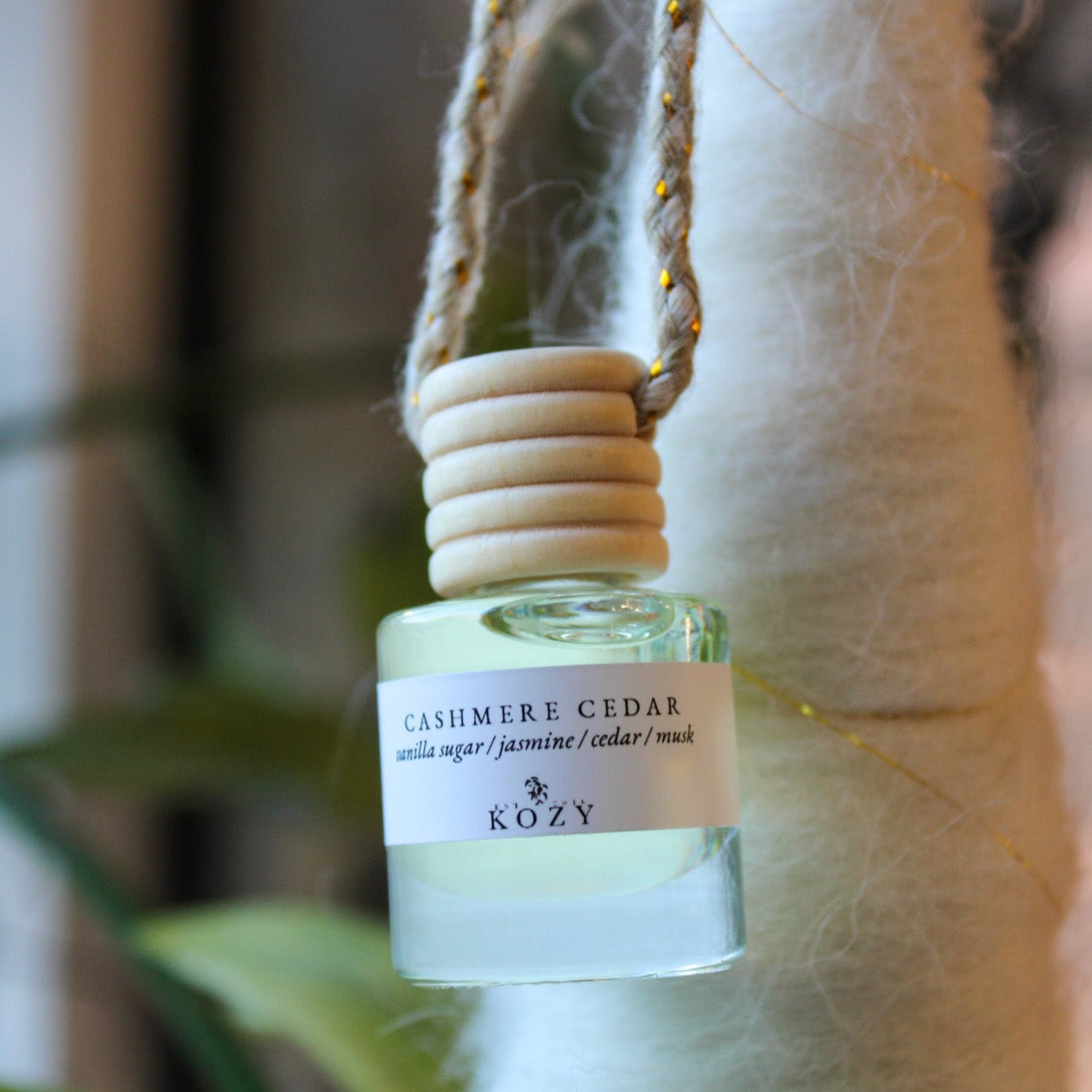 A hanging car diffuser with a label reading 'CASHMERE CEDAR' and the brand 'KOZY' on it, with a wooden cap and a vent clip.