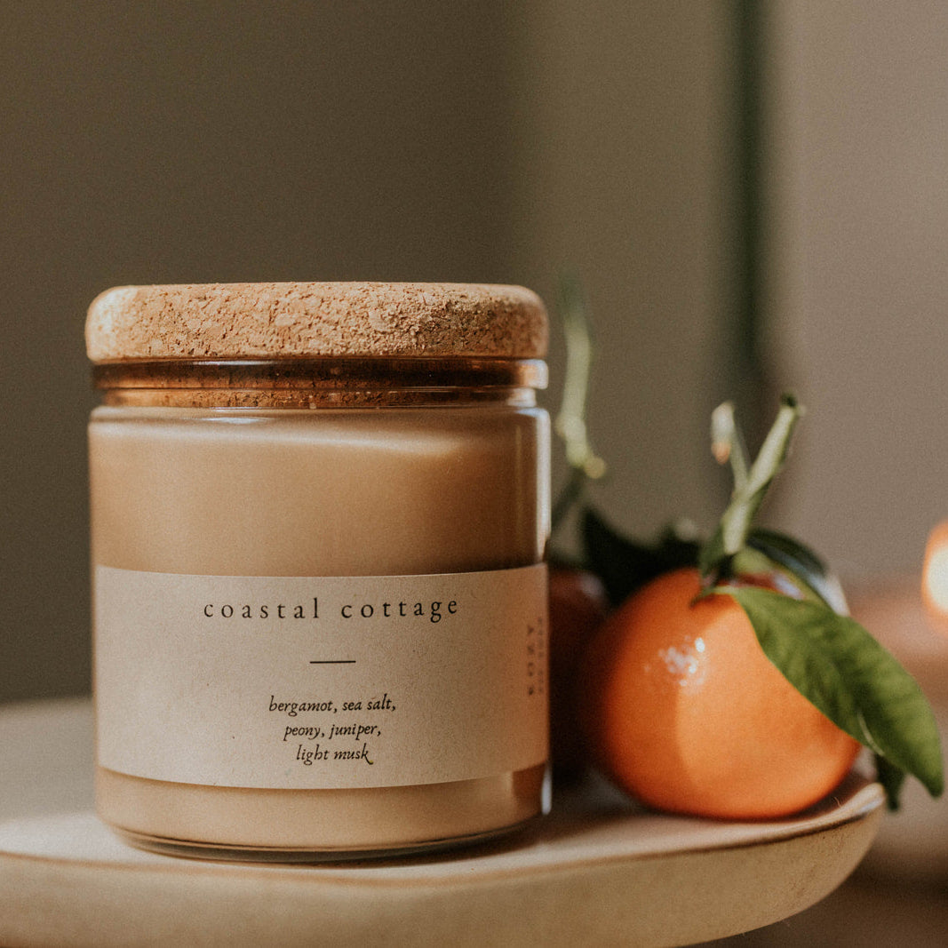 Candle labeled 'Coastal Cottage' on a plate with an orange and green leaf.