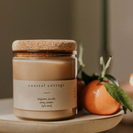 Candle labeled 'Coastal Cottage' on a plate with an orange and green leaf.
