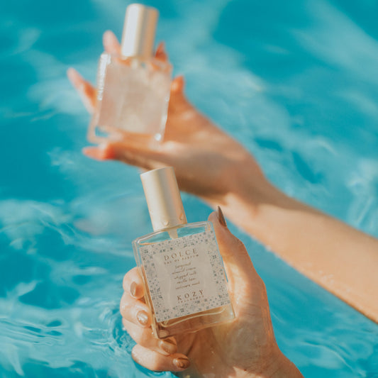 Two hands holding perfume bottles against a blue water background