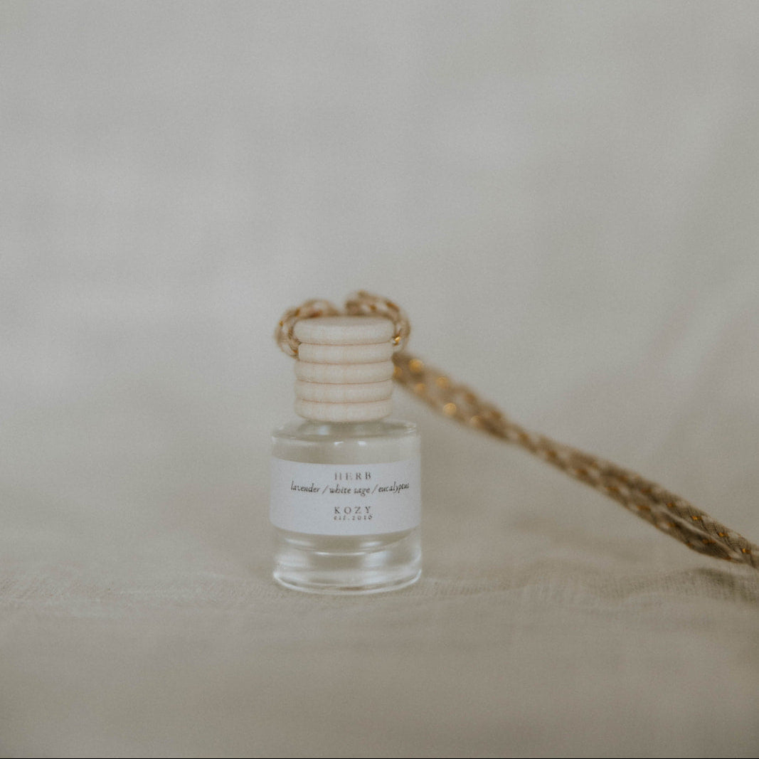 Small hanging car diffuser in the scent 'Herb' with a beige background.