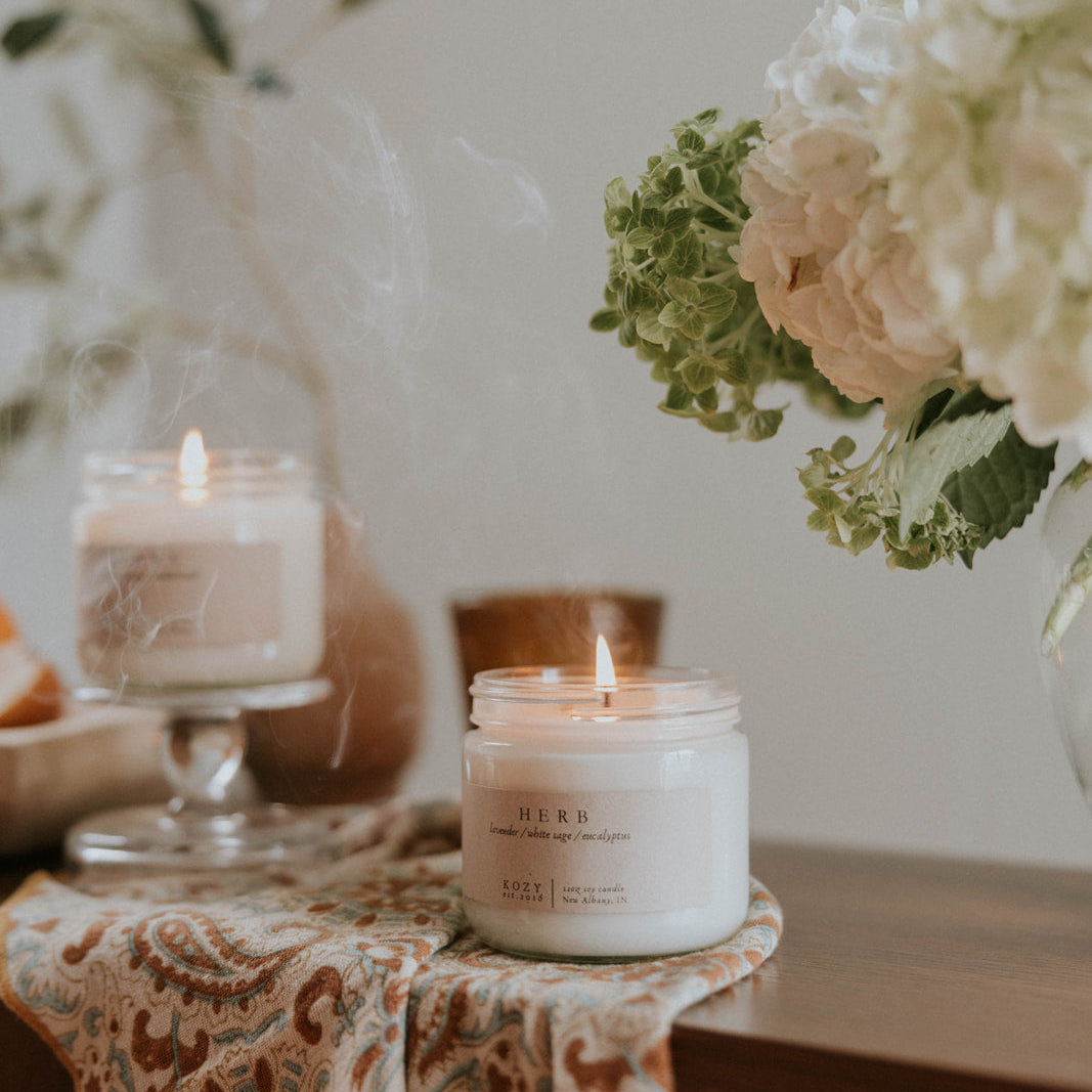 Candle on a table with flowers and a vase in the background