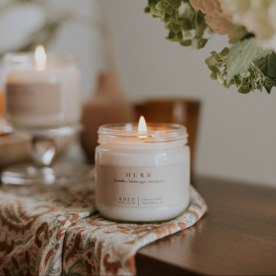 Candle 'HERB' scented on a table with flowers in the background
