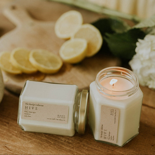 Candle and packaging on a wooden surface with lemons and flowers in the background