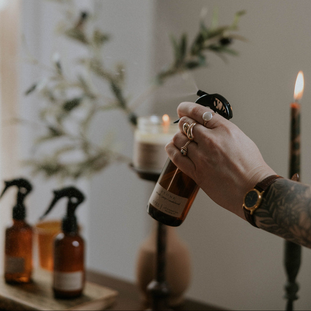 Hand holding a bottle with a blurred background of candles and plants