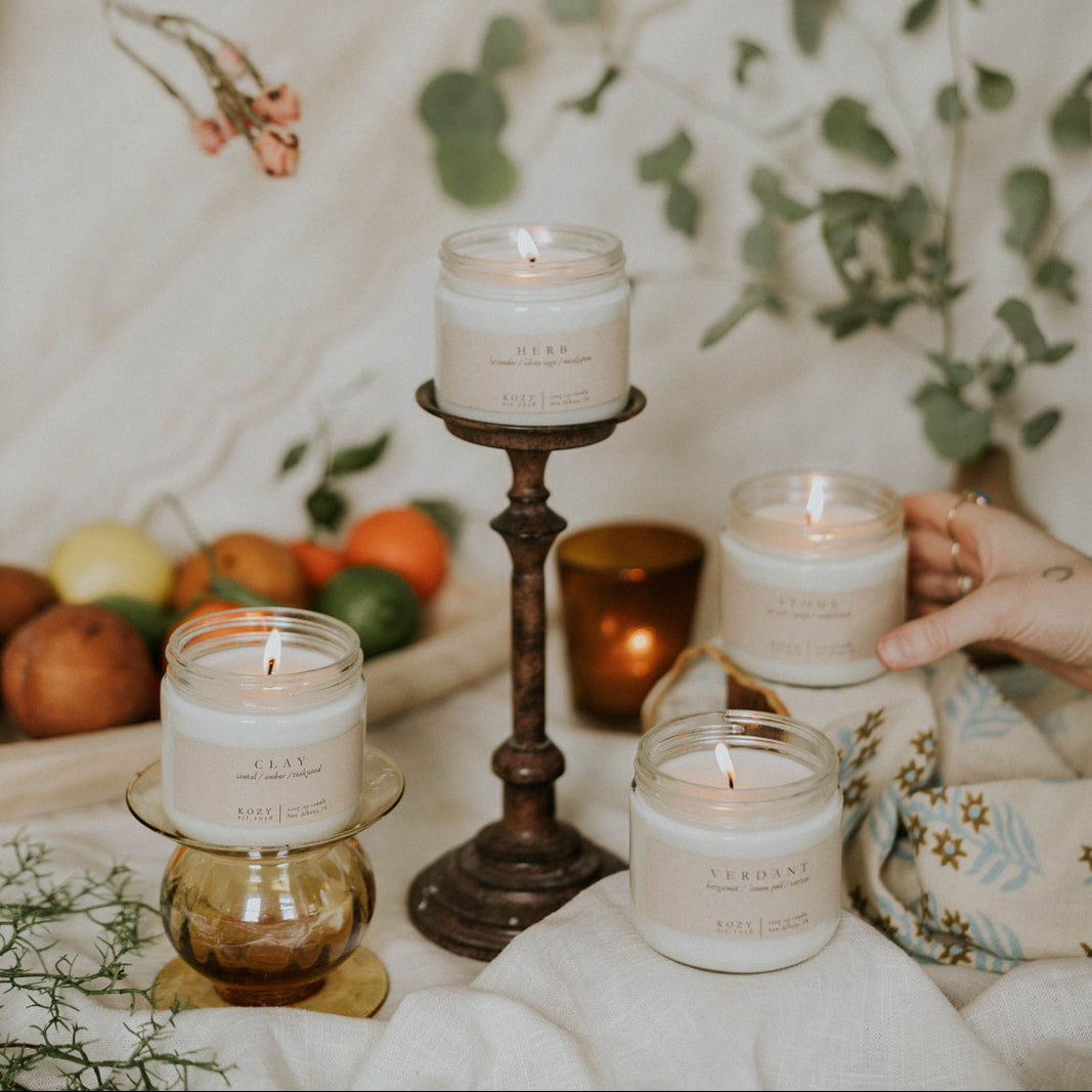 Candles on various holders with a decorative background of fruits and plants.