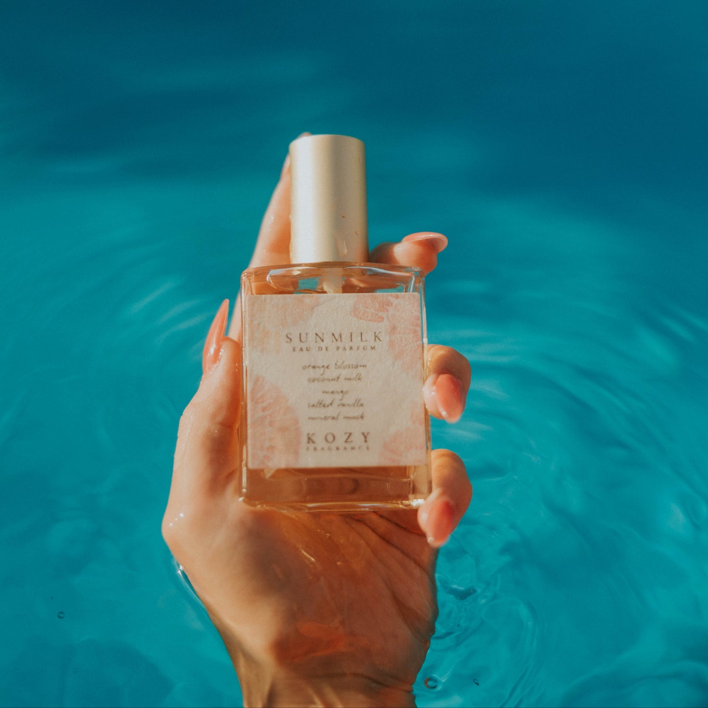 Hand holding a perfume bottle with a blue water background