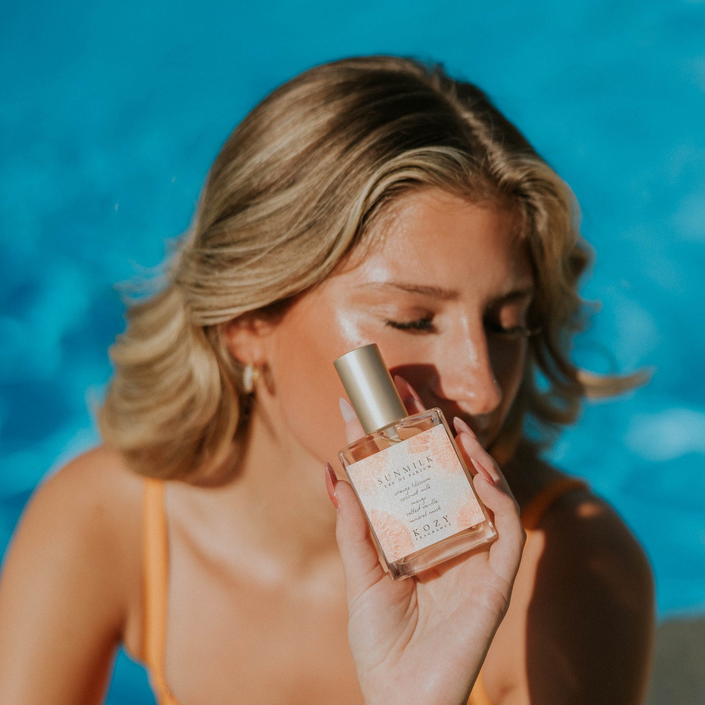 Woman holding a bottle of perfume by a pool