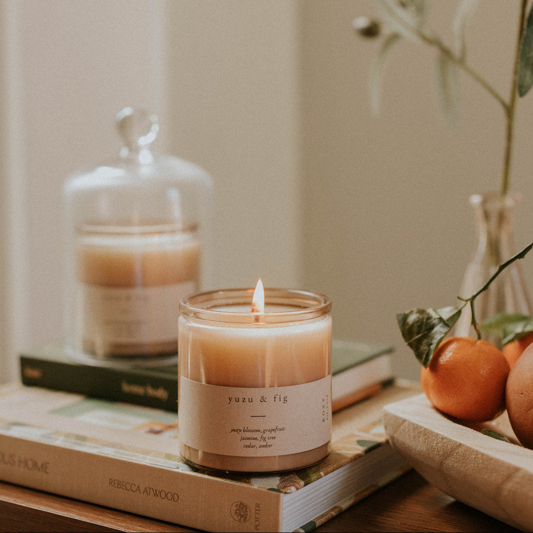 Yuzu and Fig candle, lit on a table with books.