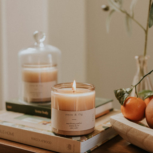 Yuzu and Fig candle, lit on a table with books.