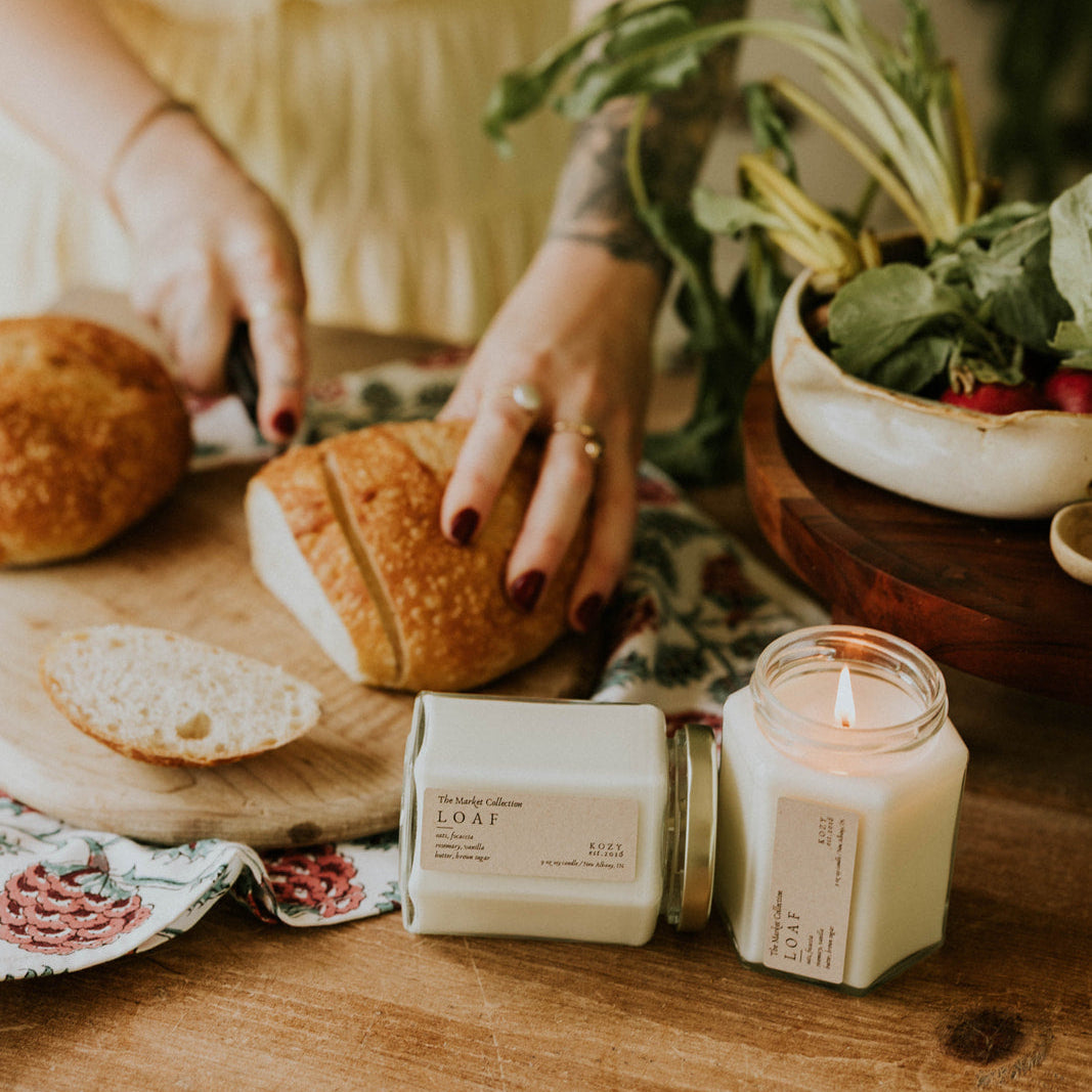 Person preparing bread on a wooden table with candles and plants
