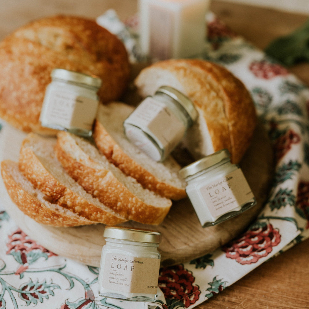 Loaf of bread with slices and jars on a decorative cloth with a candle in the background