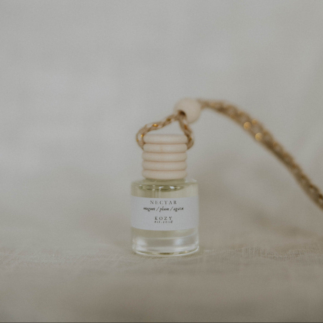 Hanging car diffuser in a small clear bottle on a beige background. The scent is 'Nectar'.