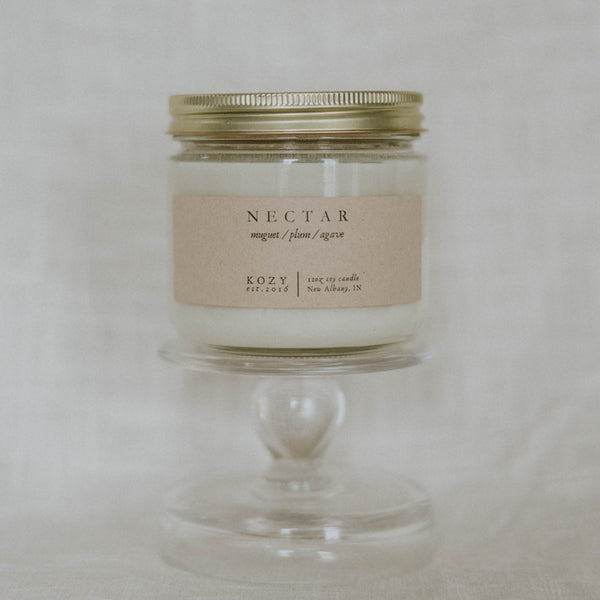 Candle in a glass jar with a gold lid on a light gray background
