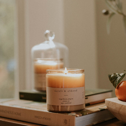 Candle labeled 'Neroli & Almond' on a stack of books, with a blurred background