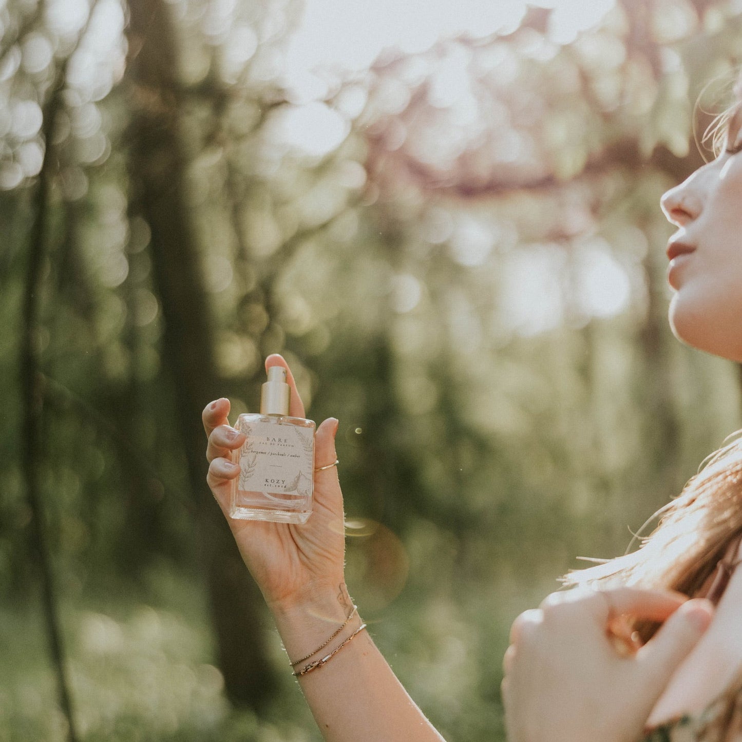 Person holding a perfume bottle outdoors with trees in the background