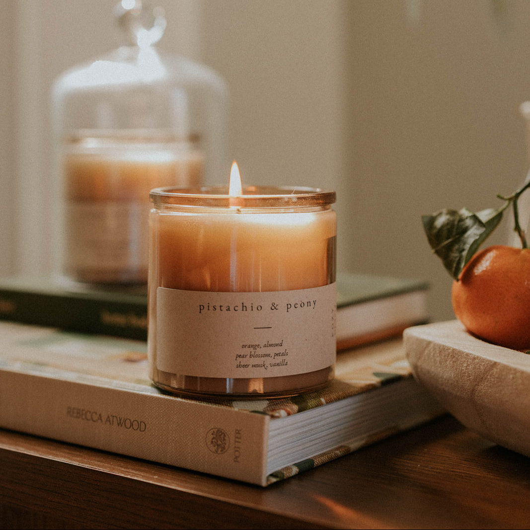 Candle with a label on a book, surrounded by books and a small plant