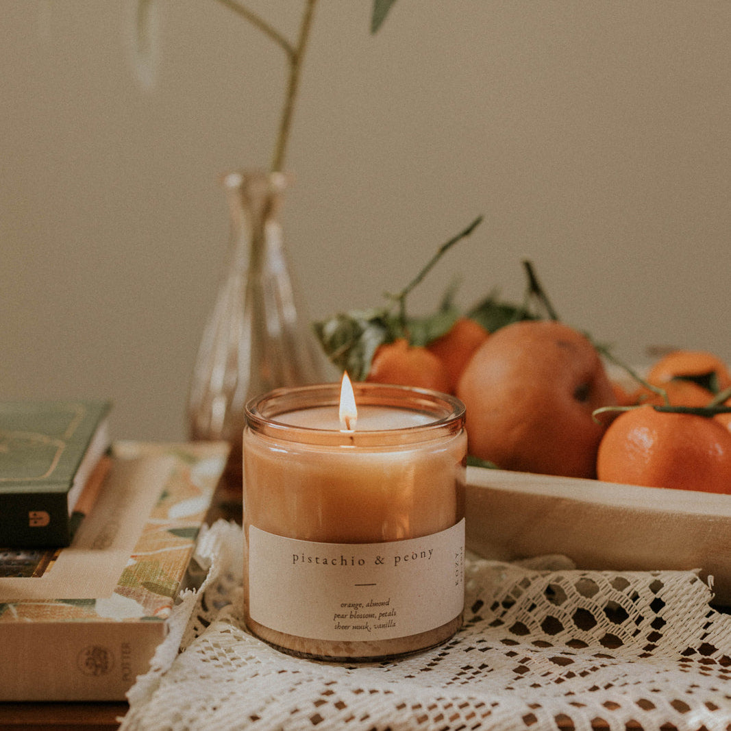 Candle with a label on a table with fruits and a plant in the background