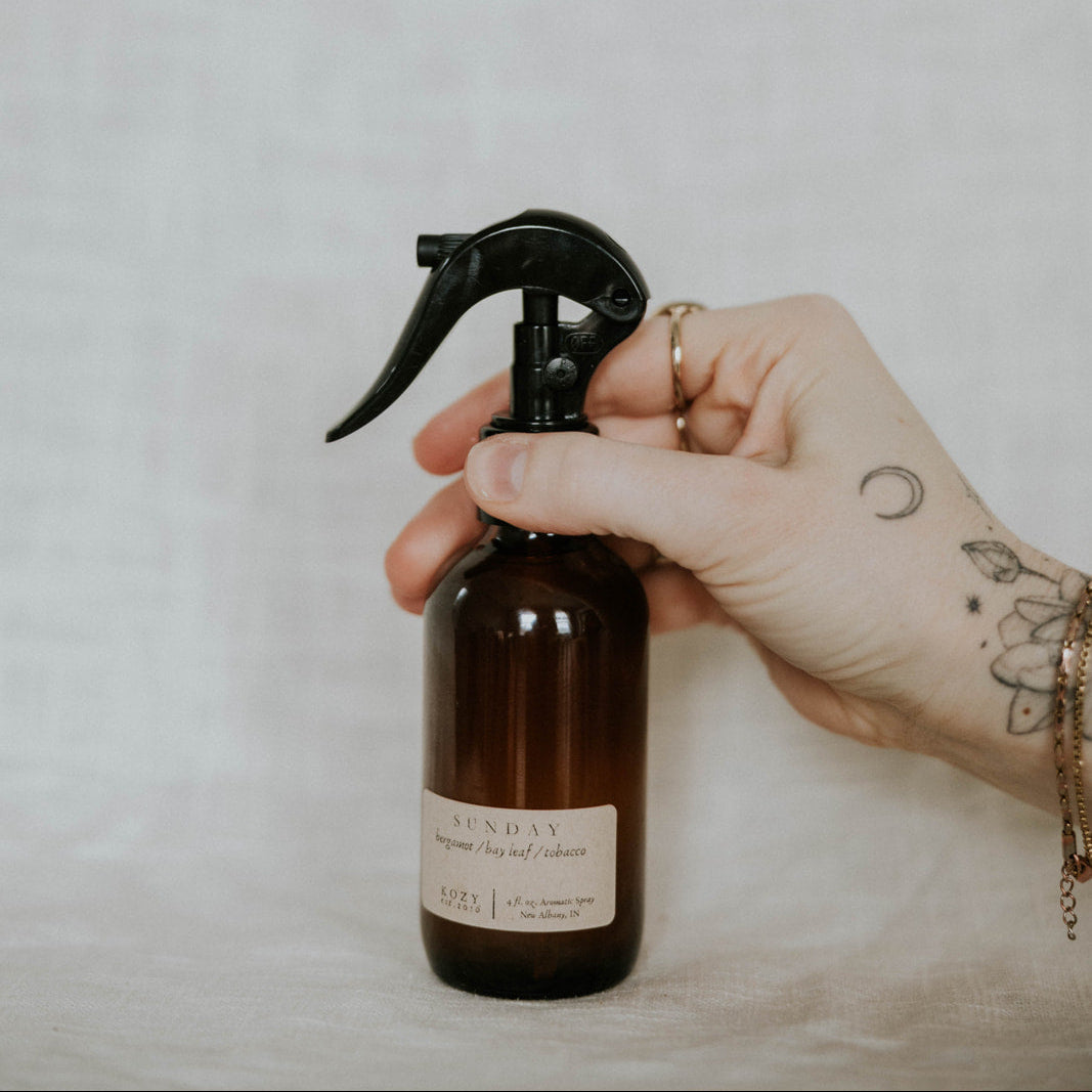 Hand holding a brown spray bottle with a black nozzle against a plain background
