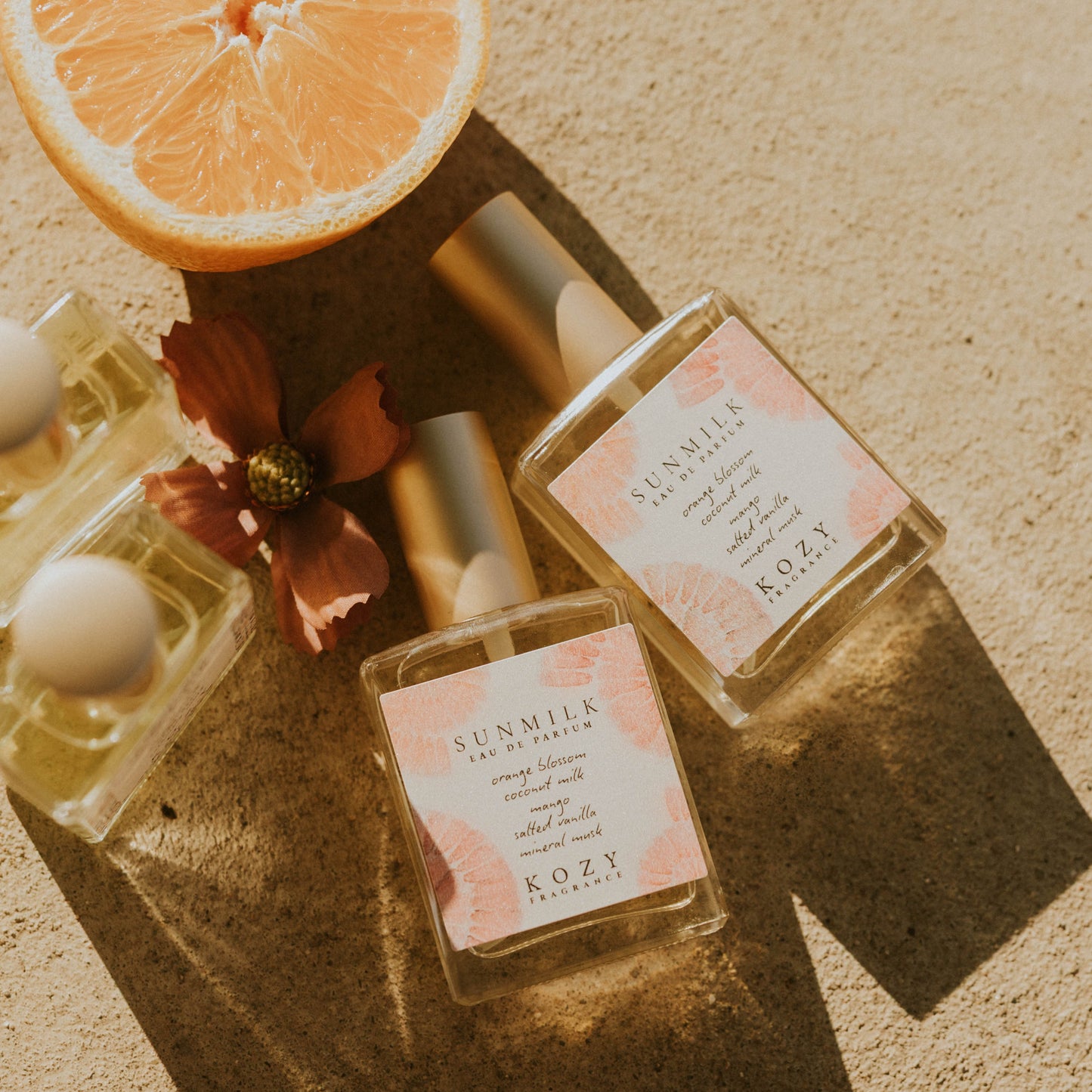 Perfume bottles with floral elements and a sliced orange on a textured surface