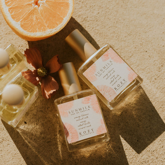 Perfume bottles with floral elements and a sliced orange on a textured surface