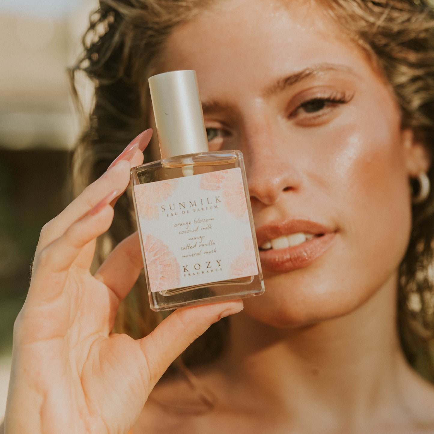 Woman holding a KOZY perfume bottle with a blurred background