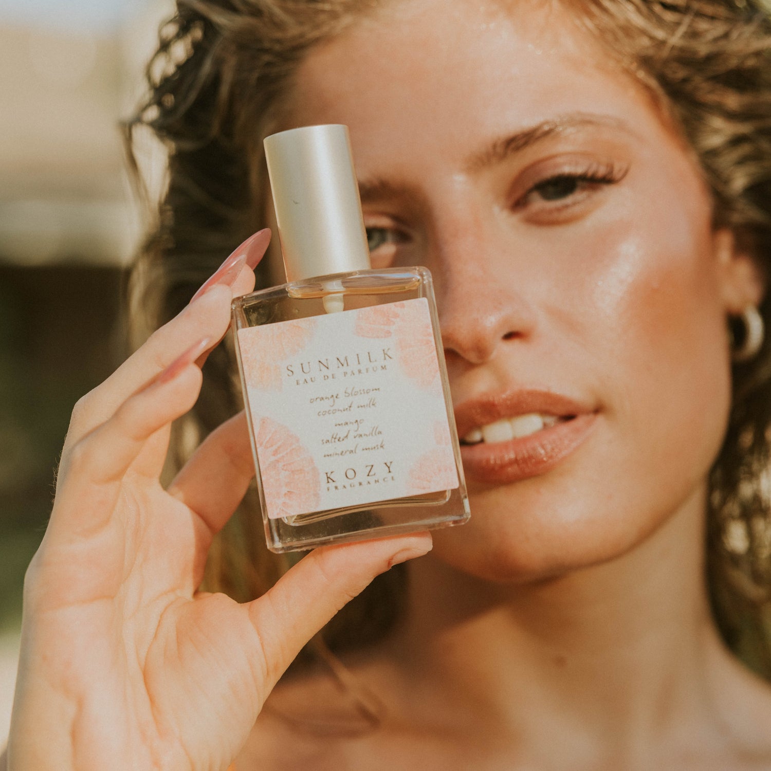 Woman holding a KOZY perfume bottle with a blurred background
