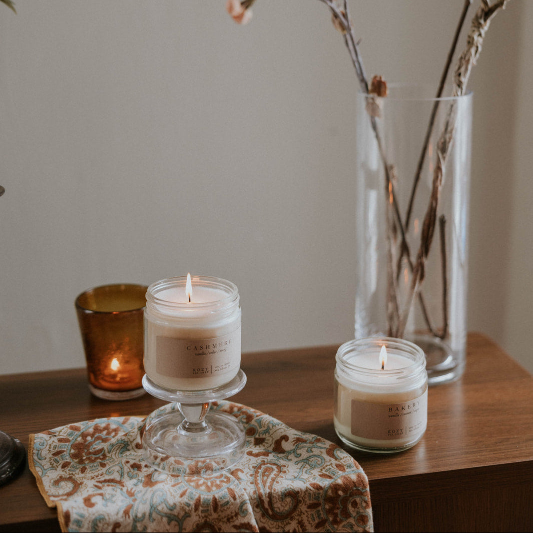 Candlelit scene with candles in glass holders and a vase with dried branches on a wooden surface.