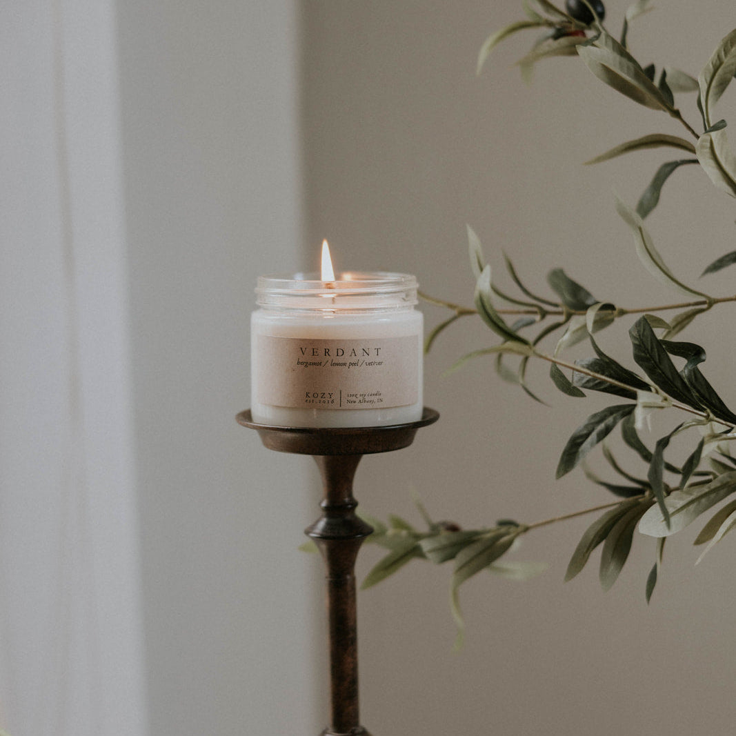 Candle in a decorative holder with greenery and pumpkins on a neutral background