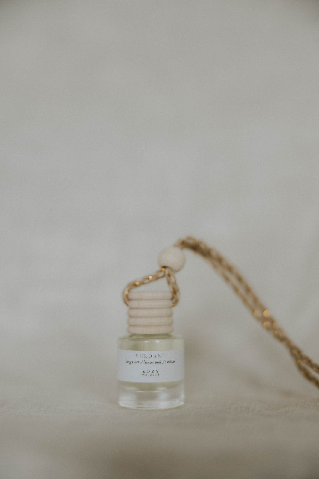 Small hanging car diffuser with a beige cap on a beige surface. The scent is 'Verdany'.