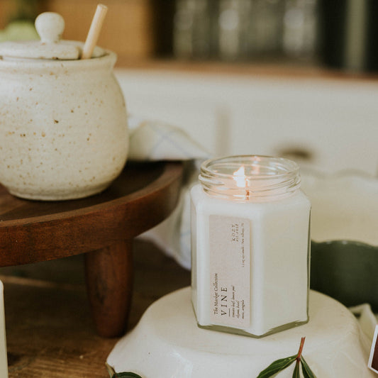 Candle in a glass jar on a white stand with green leaves, blurred background