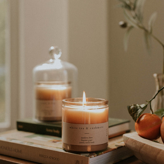 Candle on a book with a blurred background featuring books and a plant.