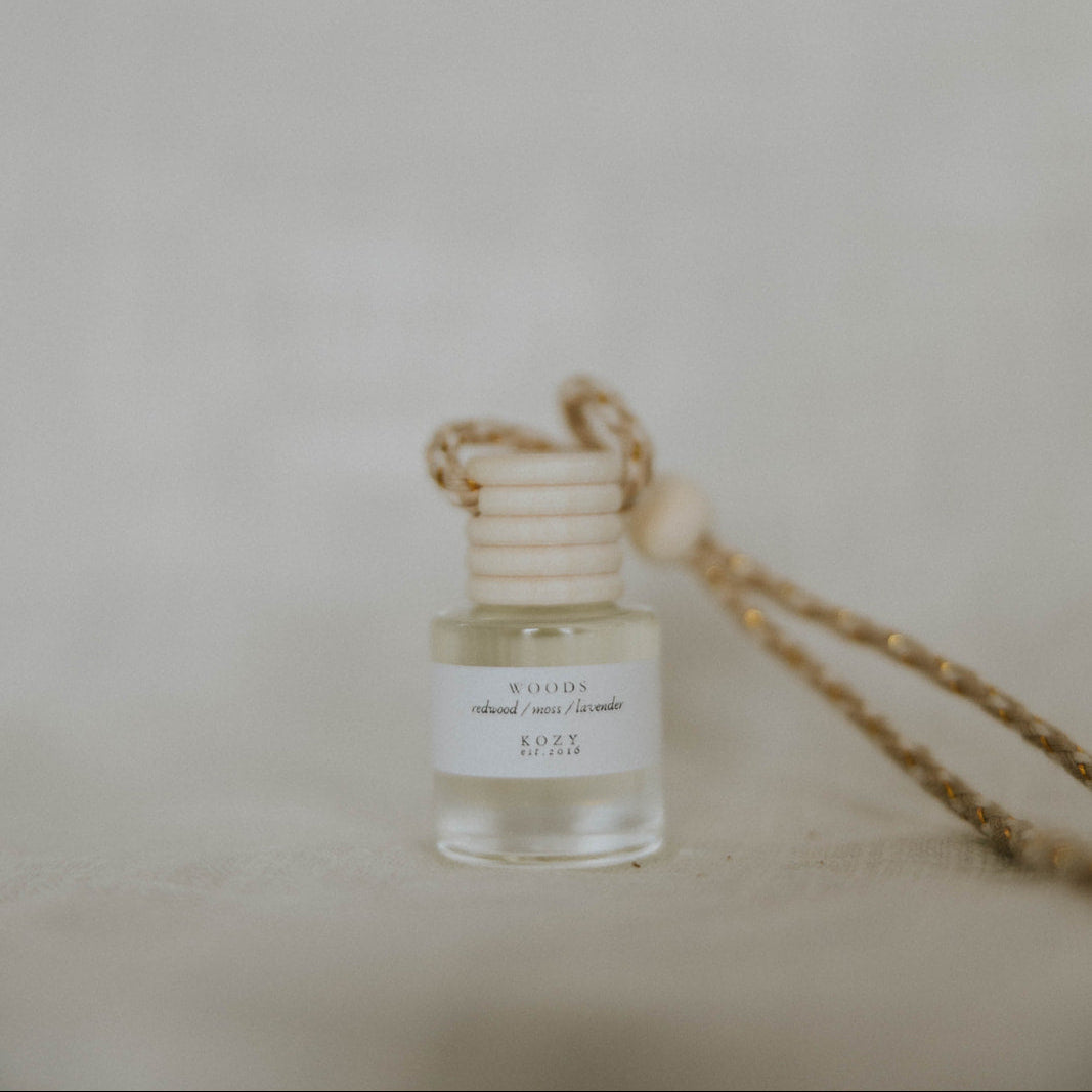 Small hanging car diffuser in scent 'Woods' with beige background.