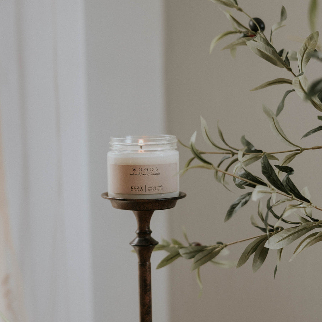 Candle in a holder with greenery and pumpkins on a neutral background