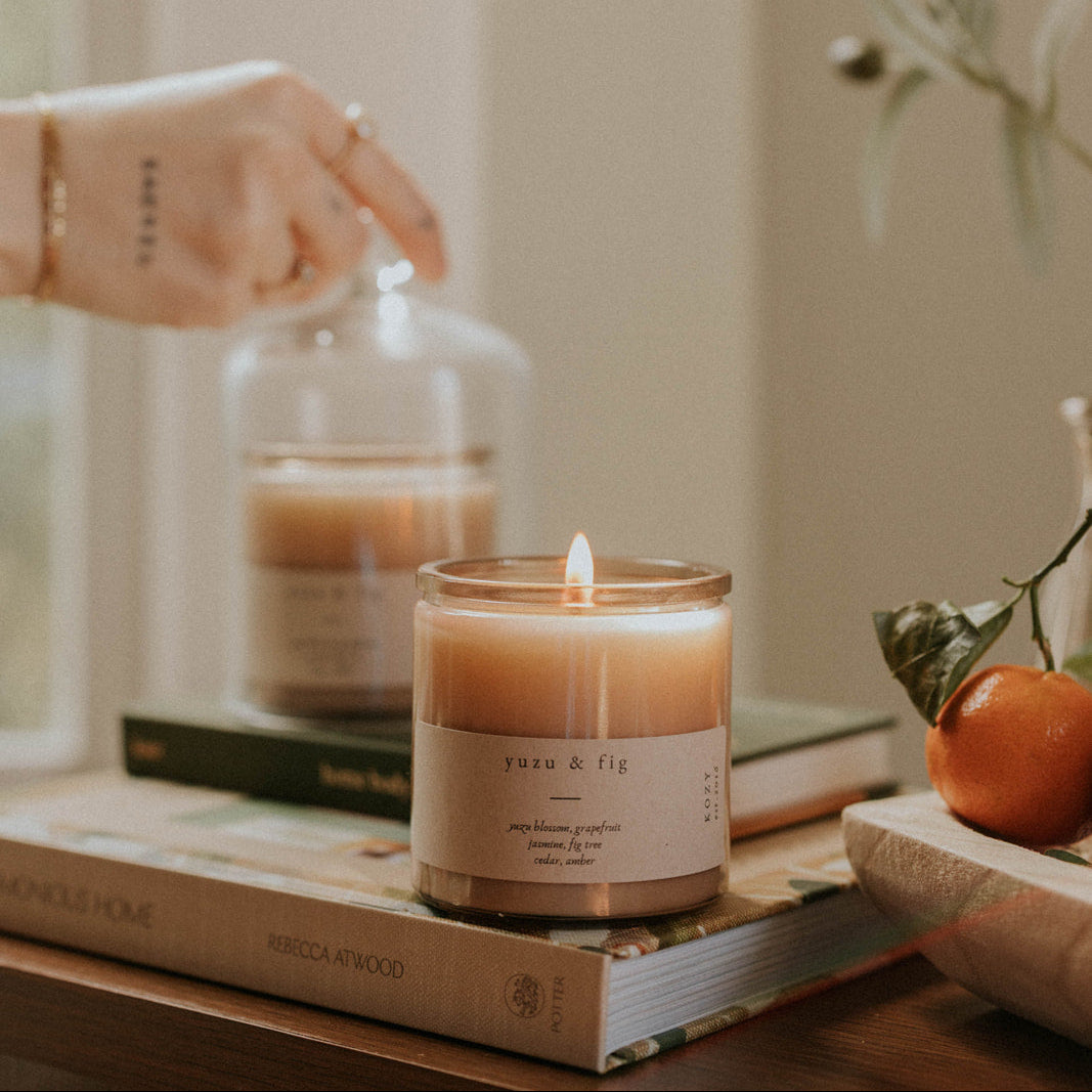 Candle being lit on a table with books and a decorative glass cloche.
